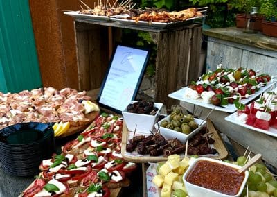 Reichhaltiges Buffet mit Tomate-Mozzarella-Spießen, Bruschetta, Oliven und verschiedenen Dips auf rustikalen Holzplattformen.