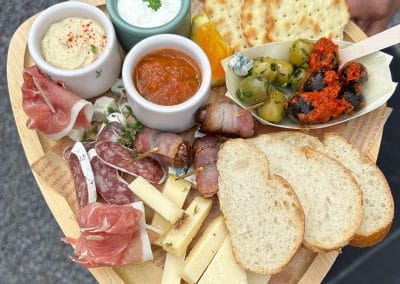 Eine herzhafte Tapas-Platte auf einem Holzbrett mit Salami, Schinken, Käse, Oliven, Dips und hellem Brot.