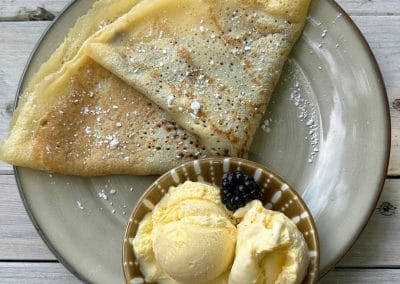 Ein Teller mit einer dünnen Crêpe und Puderzucker, serviert mit einer Kugel Vanilleeis und einer frischen Brombeere.
